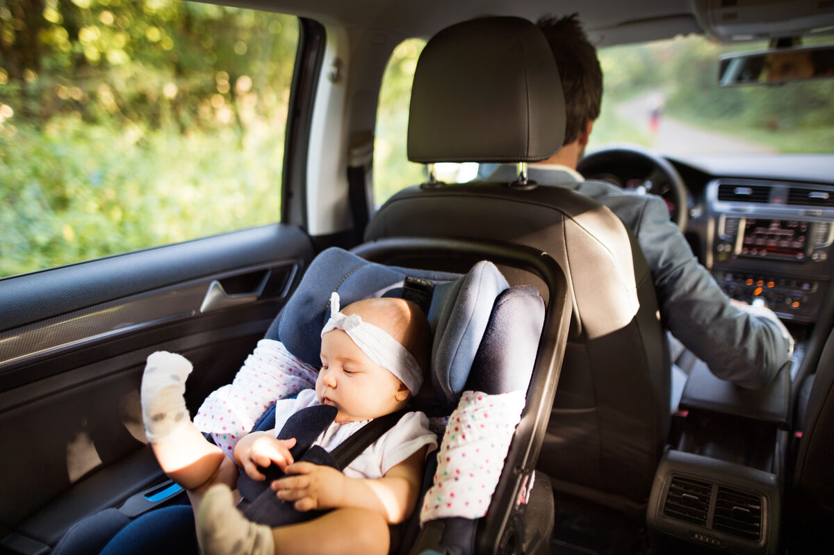 A newborn asleep in a child seat in the back of a car