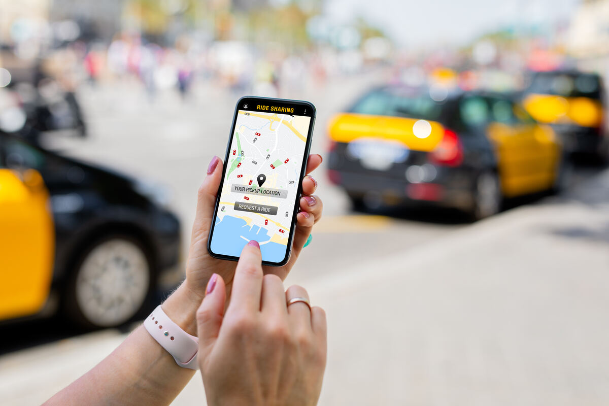 Person booking a ride on a phone with taxis in the street behind