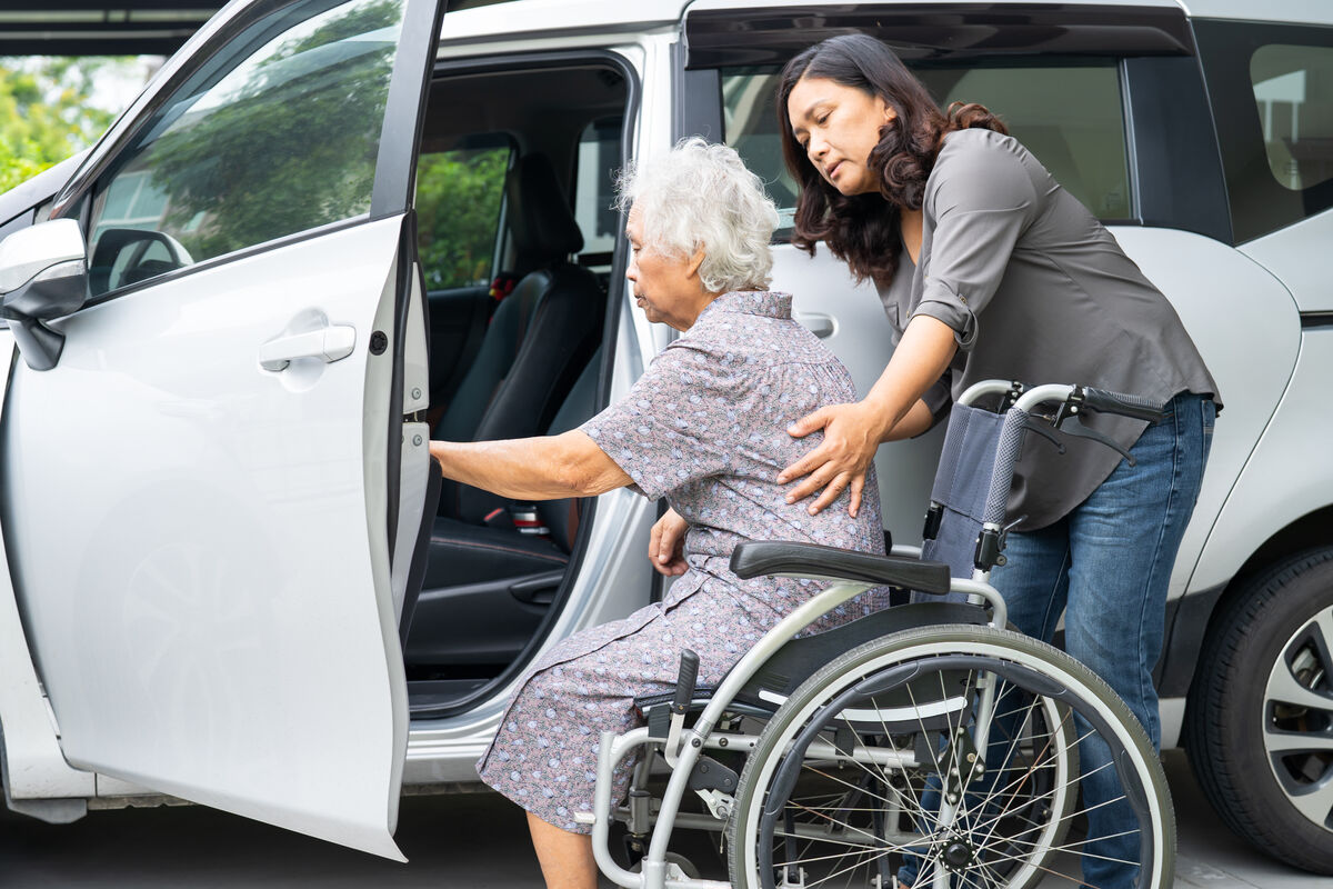 A support worker steadying a participant transferring into a vehicle