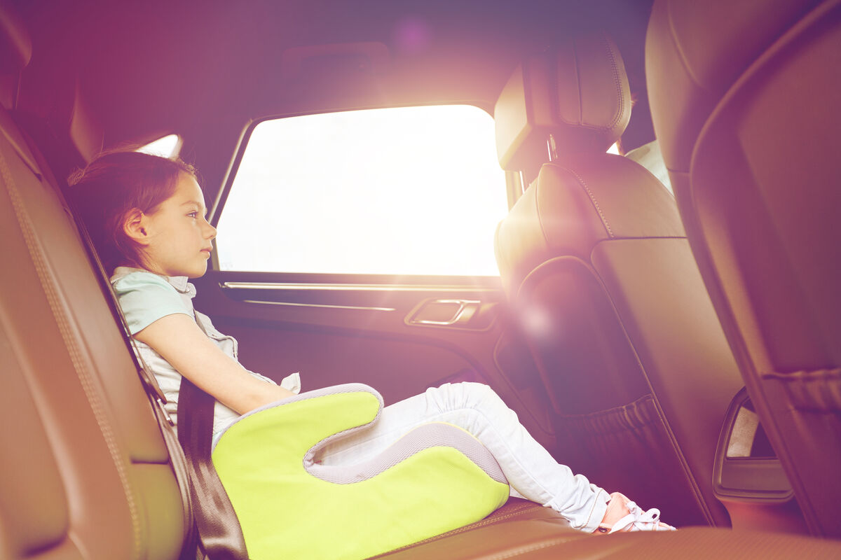 A child resting on a booster seat in the back of a car