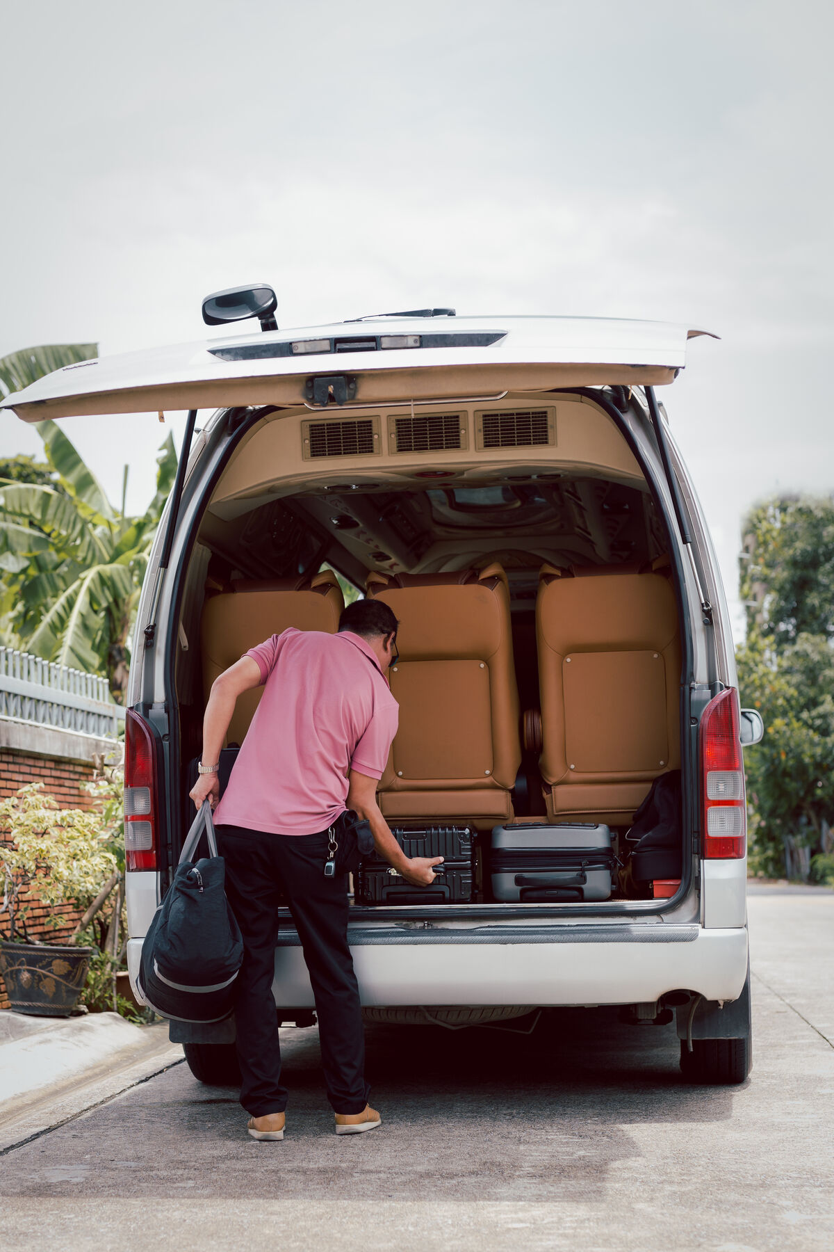 A driver lifting a suitcase into the open rear of a maxi taxi