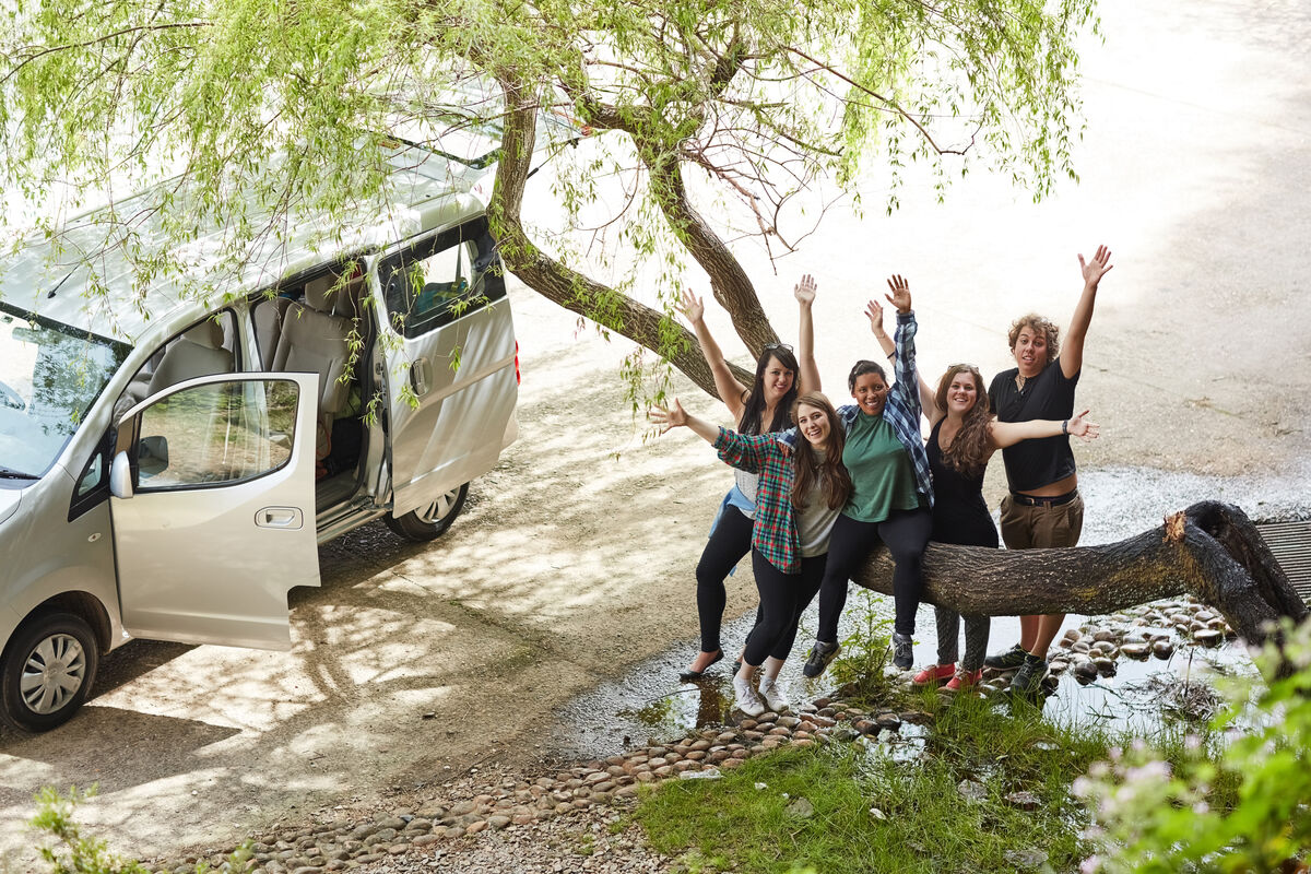 A group gathered around the open tailgate of a maxi taxi on a day out