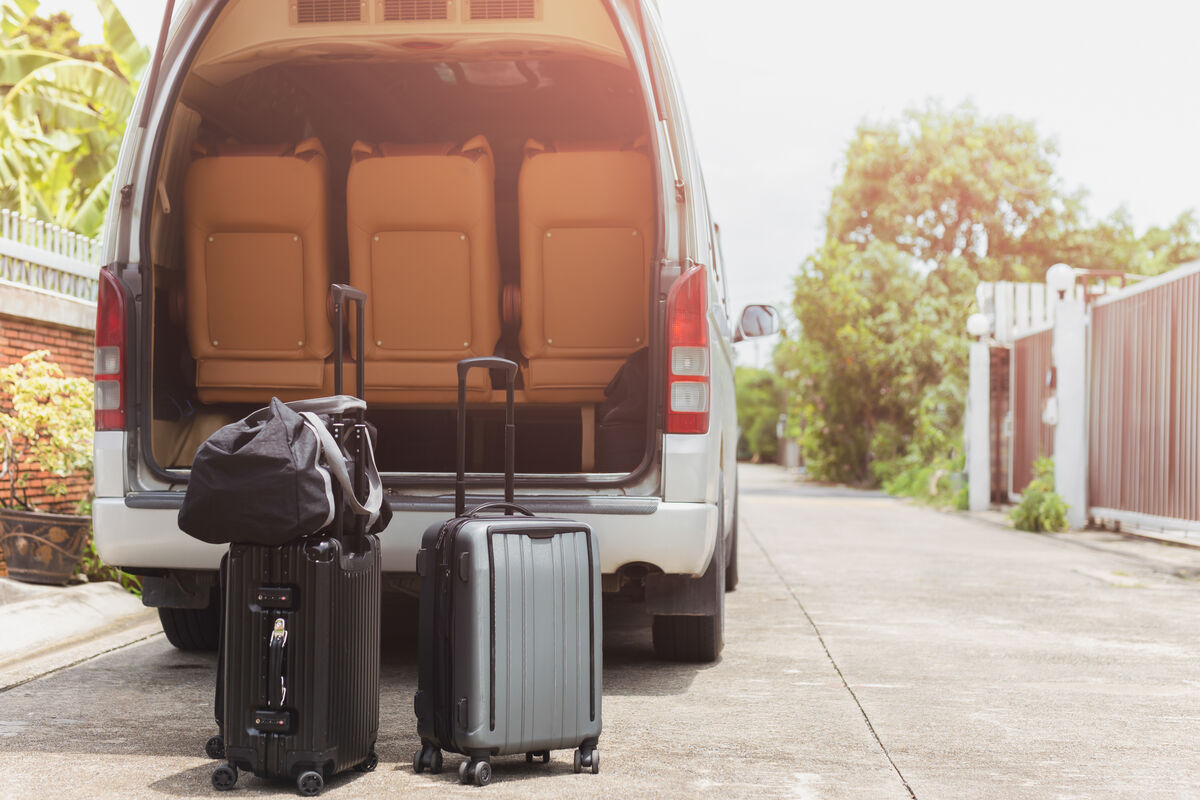 A maxi taxi with its rear doors open and suitcases standing beside it