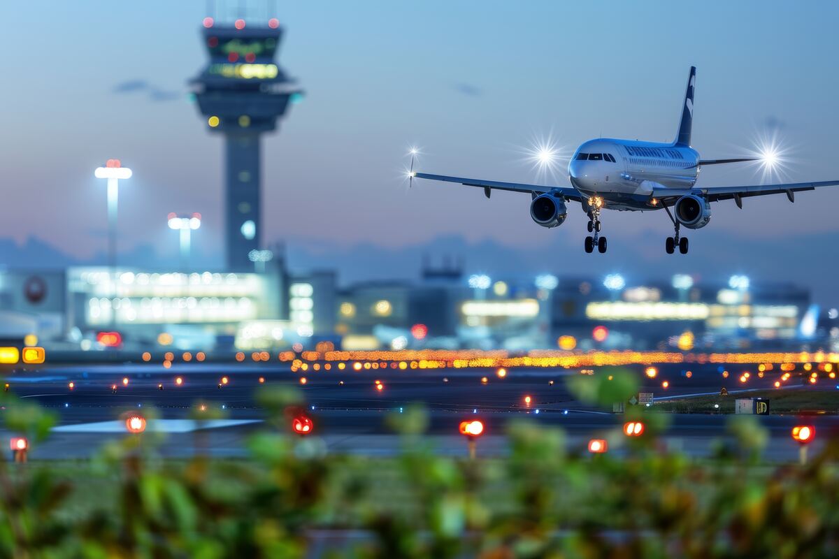 Passenger jet landing at dusk with the airport control tower and runway lights behind it
