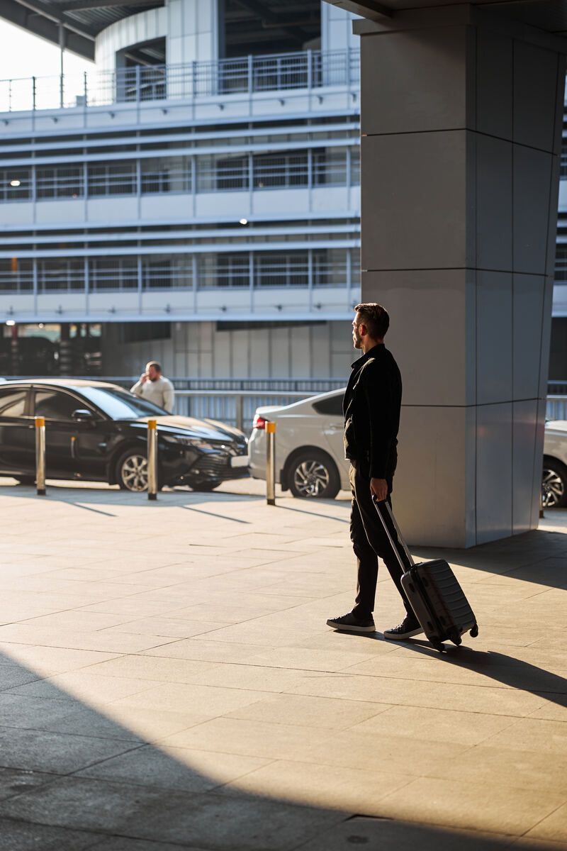 A driver waiting with a suitcase at the airport pickup area