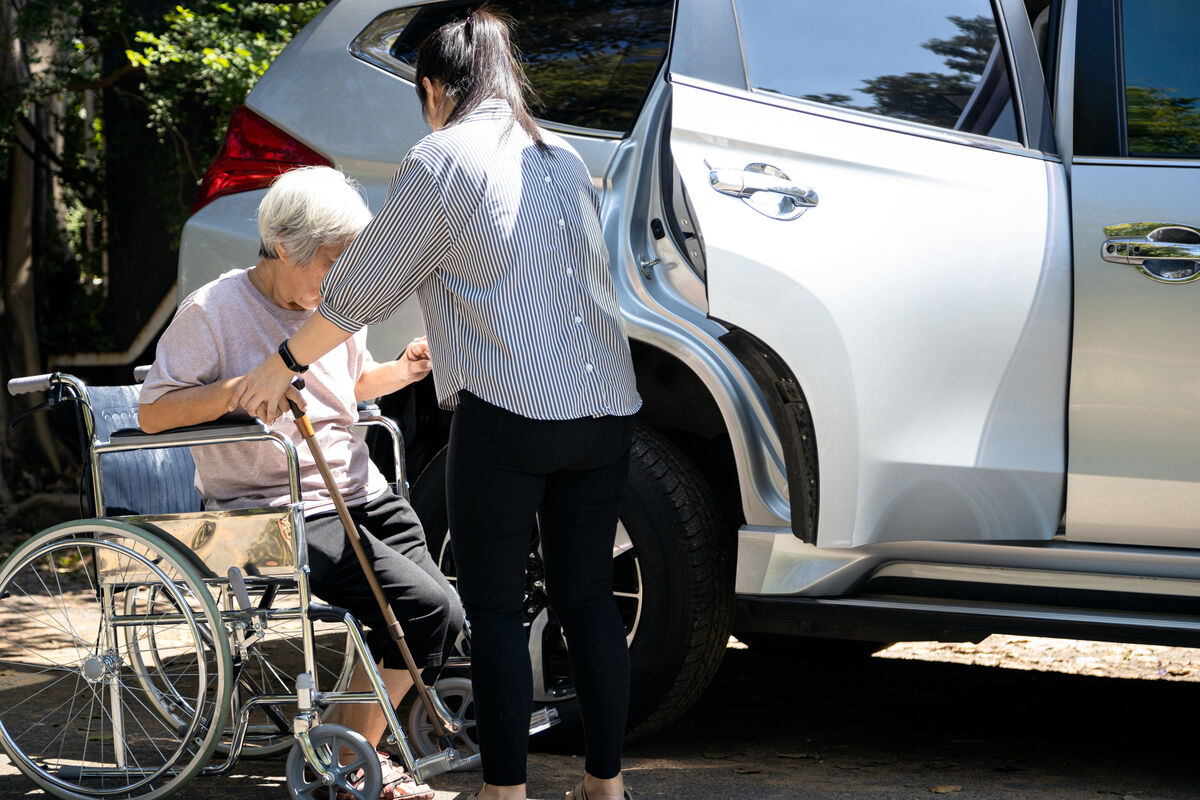 A support worker assisting a participant beside a car