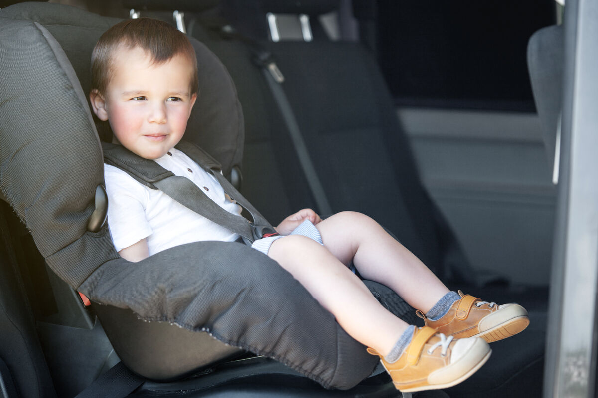 A toddler buckled into a forward-facing child seat with a harness