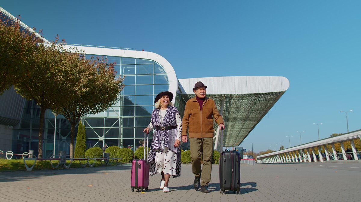 Senior couple walking with suitcases outside an airport terminal to their booked maxi cab